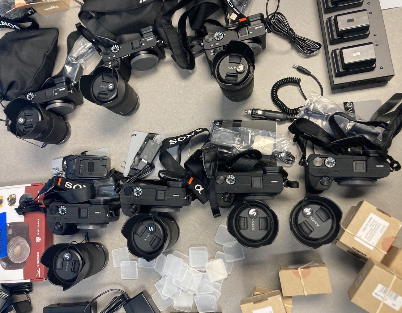 An assortment of equipment items, including cameras, lenses, batteries and packaging.