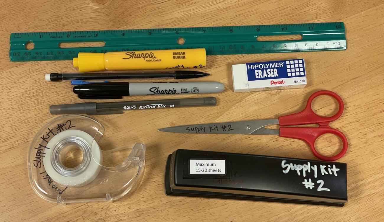 Image of supply kit contents - green plastic ruler, yellow highlighter, mechanical pencil, black Sharpie marker, black ballpoint pen, white eraser, small universal scissors, scotch tape, stapler