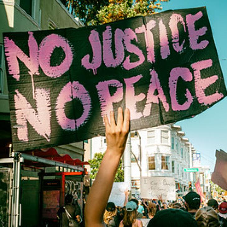An arm holding a "No Justice No Peace" sign in a Black Lives Matter march