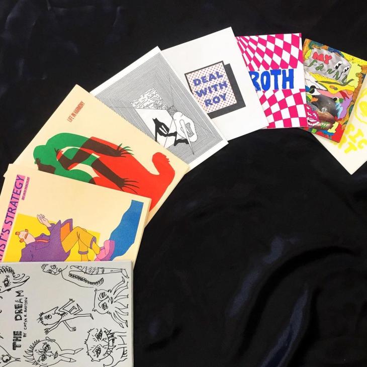 8 zines arranged in a semi circle, covers face up