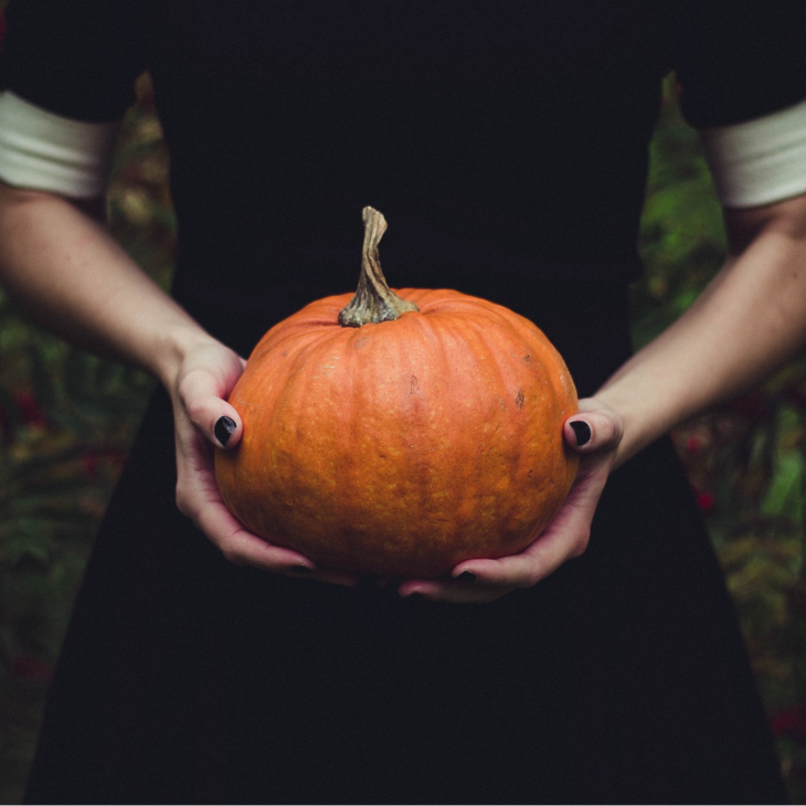 Person with black nail polish holding a pumpkin.