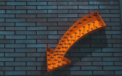 Orange arrow sign pointing down on blue brick wall