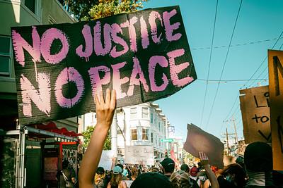 An arm holding a "No Justice No Peace" sign in a Black Lives Matter march