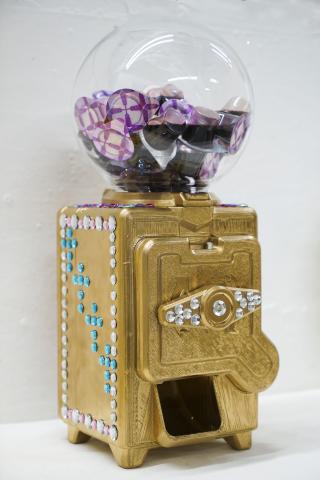 Sculpture of a gold gumball machine with rhinestones, filled with containers of sauce