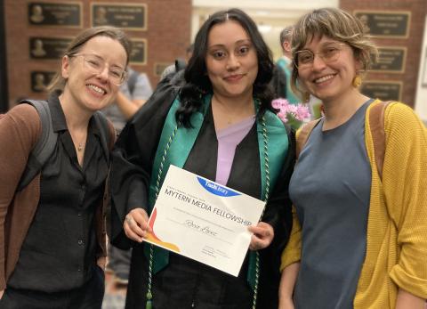 Three people pose for portrait, person in the center shows certificate