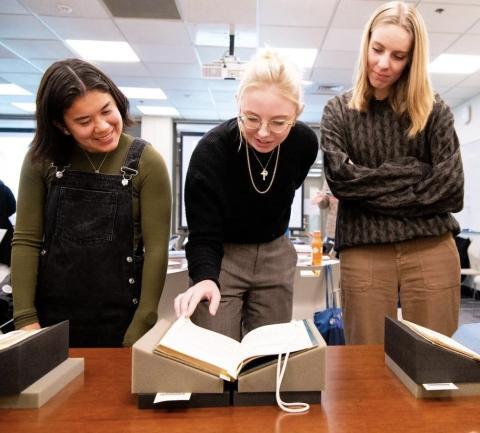 Two students and a librarian studying a rare book in class