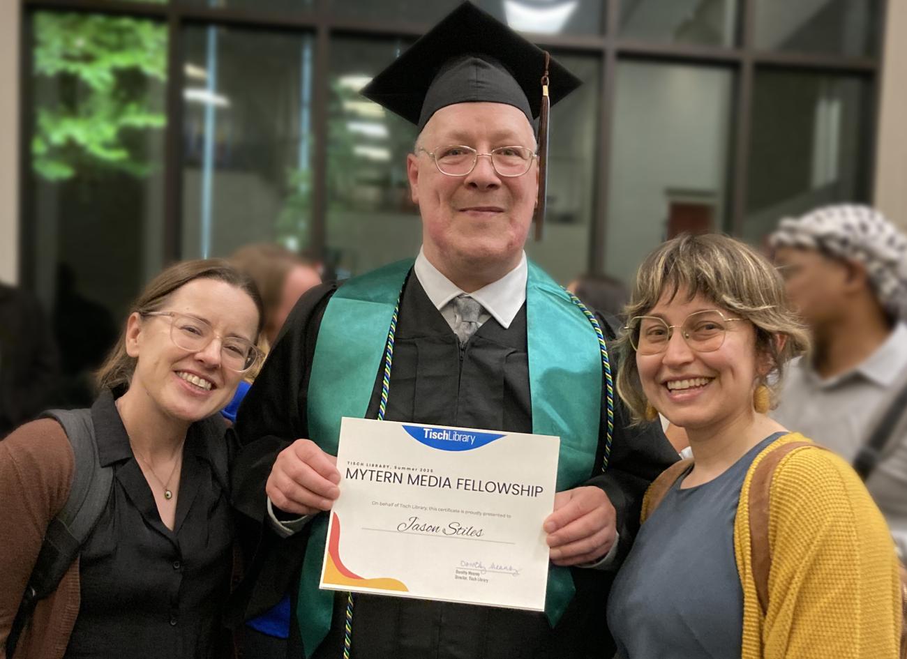 Three people posing for a portrait with middle person holding certificate