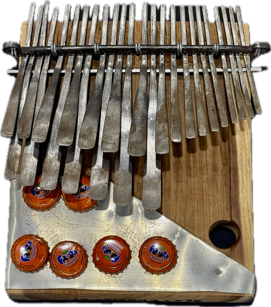 Image of a musical instrument - the mbira is sometimes called a thumb piano. The one in the images has a wooden base, metal keys in two rows along the top, and 6 bottle caps mounted on the bottom