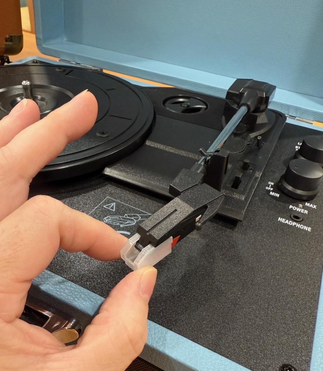 a hand is showing the plastic needle cover that needs to be removed to play records, and replaced when not in use.