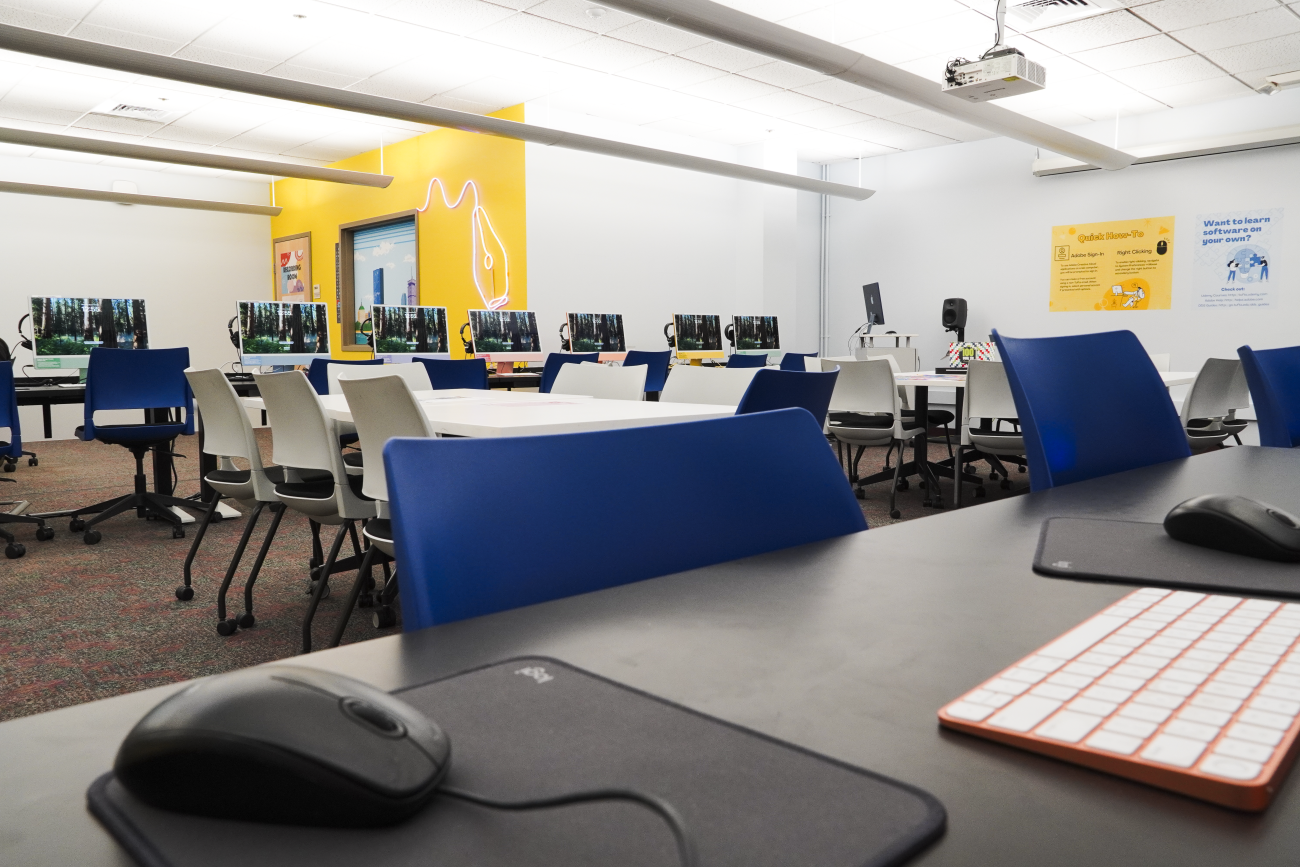 Mouse in the foreground with tables and computers against bright yellow wall in background