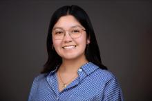Andrea Serna is pictured with a blue stripped button down, glasses, and straight dark hair.