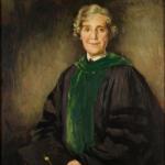 Woman wearing green academic stole holding graduate cap looking at us