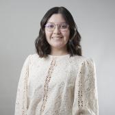 Andrea Serna is pictured with a white lace blouse, glasses, and wavy dark hair.
