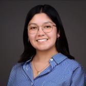 Andrea Serna is pictured with a blue stripped button down, glasses, and straight dark hair.